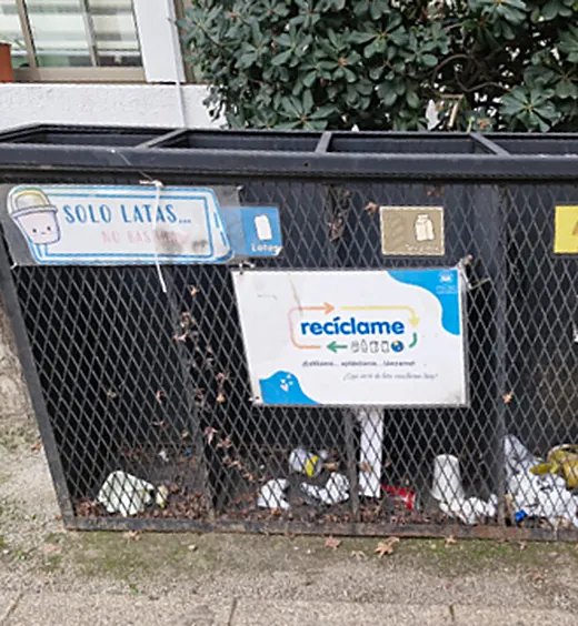 Contenedores de reciclaje del colegio con un cartel de «Solo latas» y basura de todo tipo adentro.